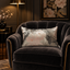 Coussin Sinapango Interiors Paris en tissage Nishijin argenté à pivoines roses, posé sur un fauteuil en velours sombre