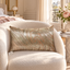 Coussin Sinapango Interiors Paris en tissage Nishijin rose poudré à tourbillon argenté, posé sur un fauteuil bouclé